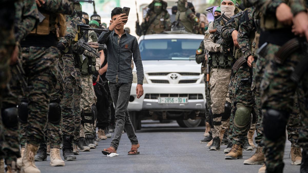 Pedestrians weave between Hamas militants as they parade through the streets for Bassem Issa, a top Hamas’ commander, who was killed by Israeli Defense Force military actions prior to a cease-fire reached after an 11-day war between Gaza’s Hamas rulers and Israel, in Gaza City, Saturday, May 22, 2021. (AP Photo/John Minchillo)
