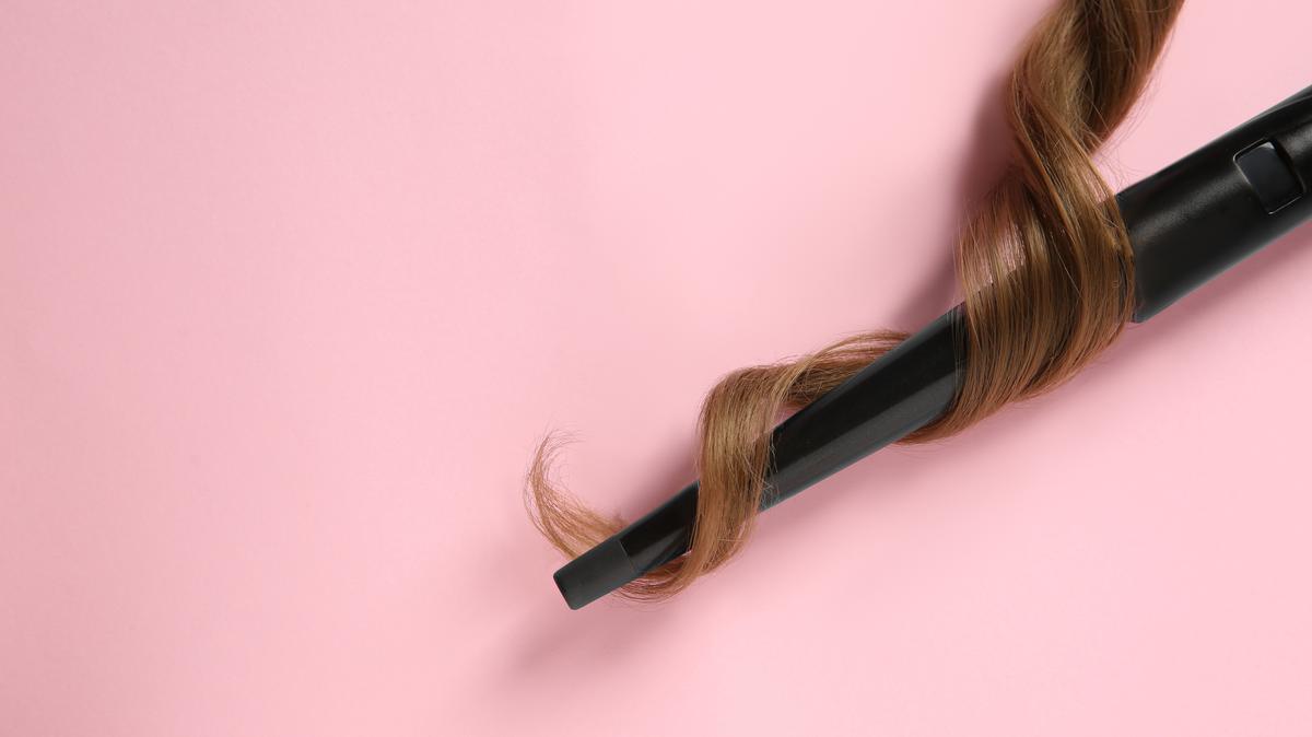 Modern clipless curling iron and brown hair lock on pink background, top view. Space for text