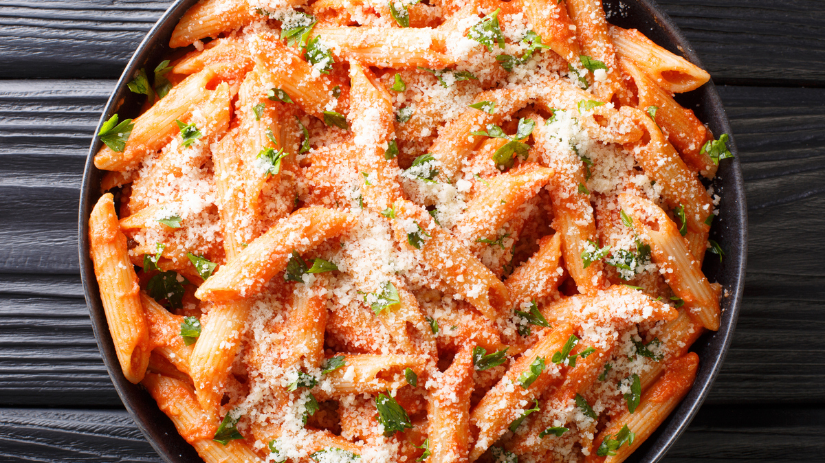 penne alla vodka is tender pasta tossed in a rich and delicious tomato, vodka and cream sauce, all topped with parmesan cheese close-up in a plate on the table. Horizontal top view from above