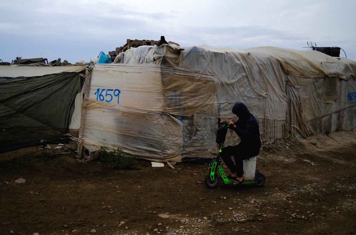 An undocumented migrant from Morocco uses an electric scooter to transport water on a canister in a shanty town after returning of his work in a plastic-covered greenhouse in Almeria province, home to Europe’s largest concentration of agricultural greenhouses, in Nijar, Spain, April 24, 2026. Undocumented migrants there live without reliable electricity and with limited access to water. REUTERS/Nacho Doce