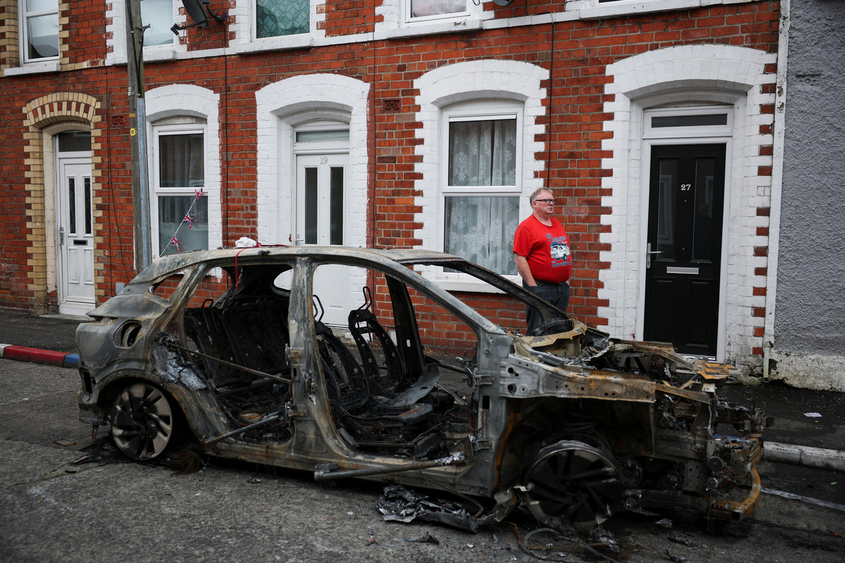 A resident stands next to a burnt car on a street in his neighbourhood, in the aftermath of anti-immigrant protests following a knife attack on June 8, which left a man seriously injured and prompted police to declare a critical incident, at Lendrick Street, east Belfast, Northern Ireland, June 10, 2026. REUTERS/Isabel Infantes