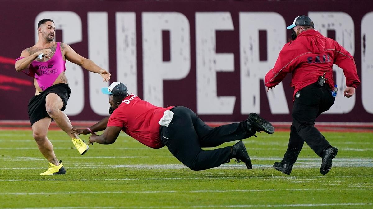 ARCHIVO.- Foto del 7 de febrero del 2021, un guardia de seguridad intenta detener a un aficionado que ingresó al campo durante el Super Bowl. El martes 27 de abril del 2021, un juez desestima el acuerdo con la fiscalía de los dos hombres que planearon y se metieron al campo. reagenda el caso para el próximo mes. (AP Photo/Mark Humphrey)