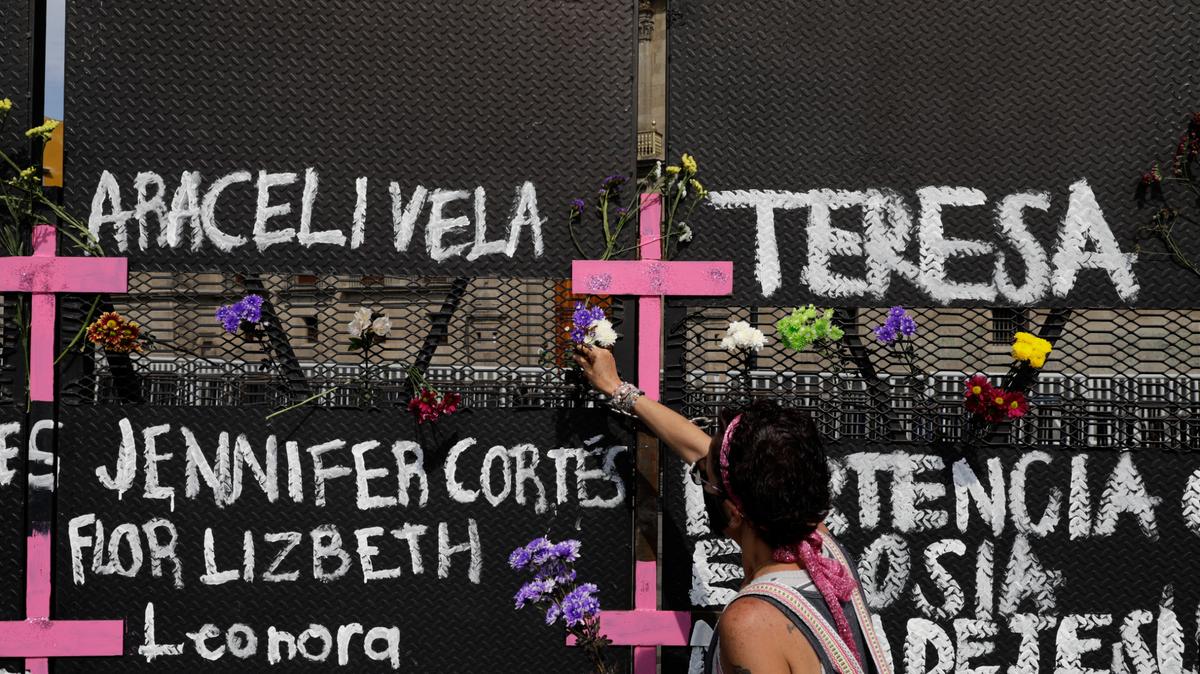 Una persona coloca flores en una valla colocada afuera del Palacio Nacional previo al Día Internacional de la Mujer, en Ciudad de México, el 7 de marzo de 2021. Activistas escribieron en la valla los nombres de mujeres desaparecidas y muertas. (AP Foto/Eduardo Verdugo)