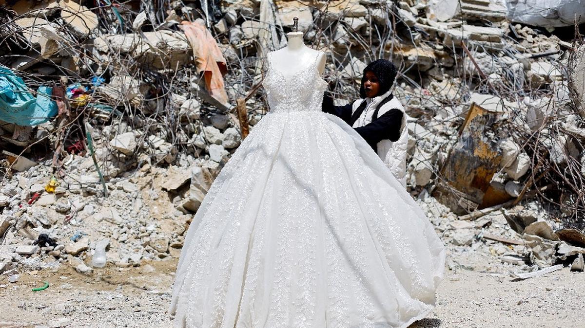A Palestinian woman looks at a wedding dress displayed outside a shop next to a pile of rubble, as brides in Gaza turn to reused gowns amid soaring prices and shortages caused by the war, in Khan Younis in the southern Gaza Strip, May 9, 2026. REUTERS/Mahmoud Issa