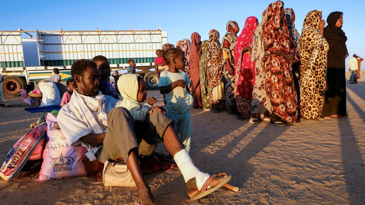 An injured man from al-Fashir sits on the ground surrounded by his children after their arrival and displaced women stand in line as they wait for their turn to receive aid, at a displacement camp in Al-Dabba, Sudan, November 19, 2025. REUTERS/El Tayeb Siddig/File Photo