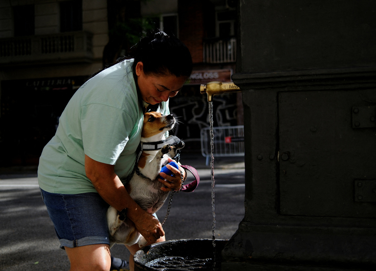 Joana cools her dog Oli in a fountain as temperatures rise, during a heatwave affecting a large part of Spain, in Barcelona, Spain, June 21, 2026. REUTERS/Nacho Doce