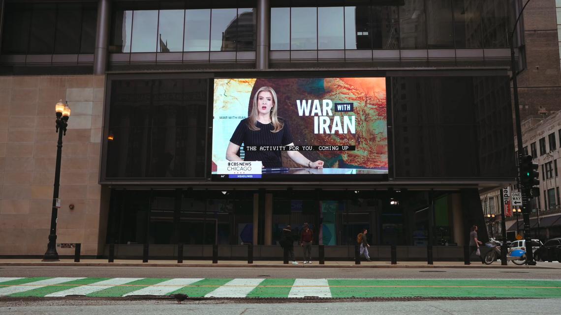 A screen showing news coverage of the war in Iran, on the side of a building in downtown Chicago in April 2026. Public-opinion surveys show that roughly six in 10 Americans oppose the U.S.-led war against Iran; some say they are simply baffled by a conflict that they feel the president did not prepare them for and that still has not been clearly explained. (Jamie Kelter Davis/The New York Times)
