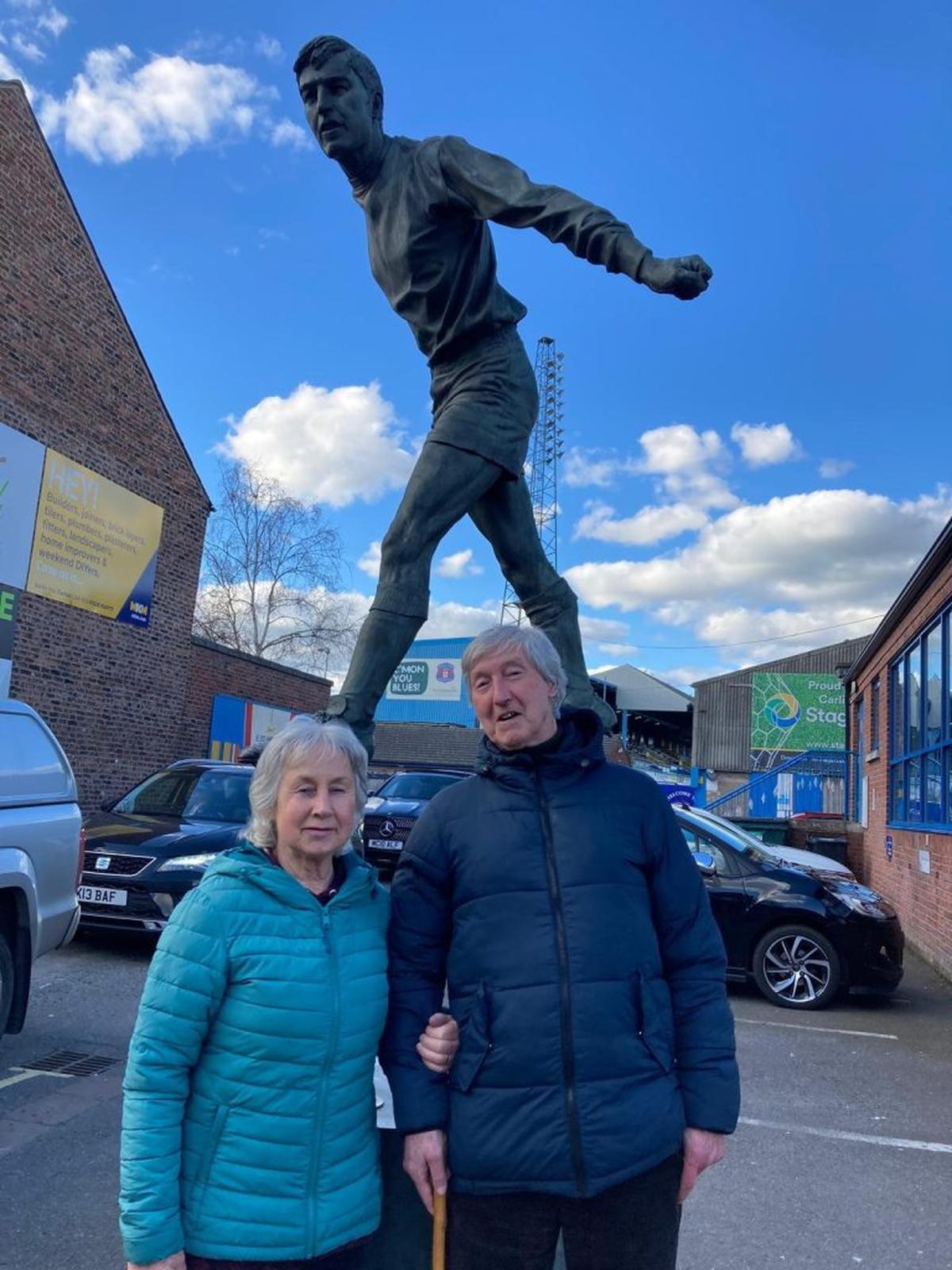  Hugh "Hughie" McIlmoyle with wife Rosalyne in front of a statue of Hugh "Hughie" McIlmoyle outside Brunton Park, the home of Carlisle United. (Alan McIlmoyle via SWNS) 