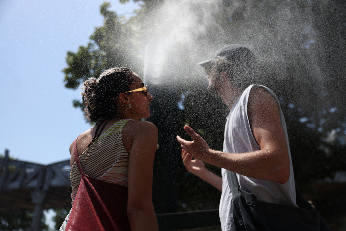 Two persons cool off at a water mister on a street in Paris as temperatures rise during a heatwave affecting a large part of France, June 22, 2026. REUTERS/Alice Sacco