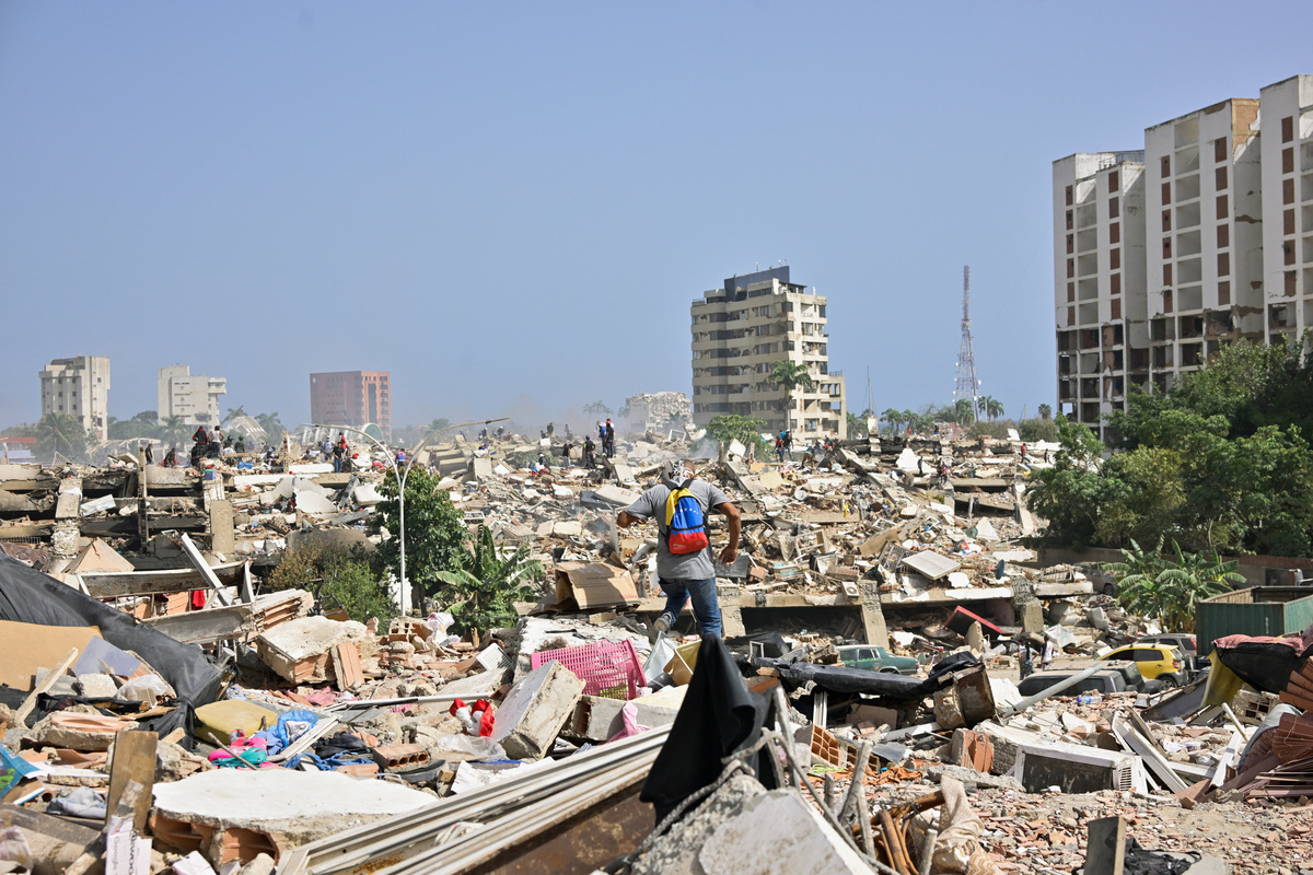 A man with a Venezuelan flag-themed backpack walks amid rubble of collapsed buildings after earthquakes hit the country, in La Guaira, Venezuela, June 26, 2026. REUTERS/Maxwell Briceno