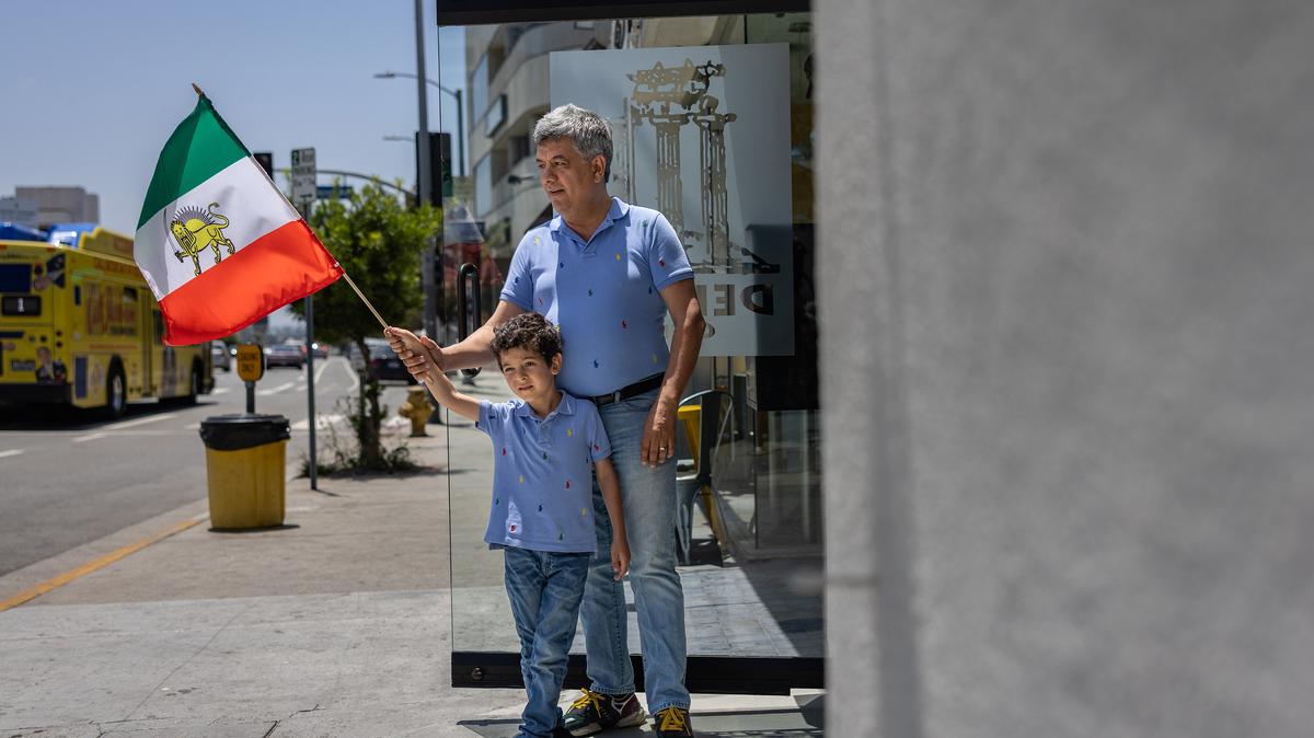 Roozbeh Farahanipour and his son Damavand wave a pre-revolution Iranian flag outside Farahanipour’s Delphi Greek restaurant on June 22, 2025, in the Westwood neighborhood of Los Angeles. (Jason Armond/Los Angeles Times/TNS)
