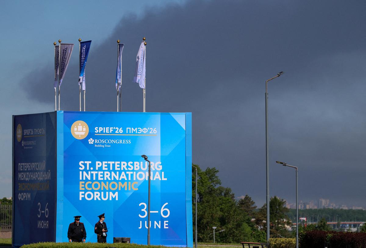 Police officers stand in front of a banner and flags with the logo of the St. Petersburg International Economic Forum (SPIEF) as heavy smoke billows in the background after drones hit infrastructure, according to the governor Alexander Beglov, in St Petersburg, Russia June 3, 2026. REUTERS/Stringer