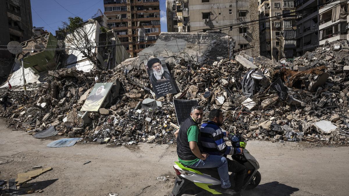 Men pass a poster of Ayatollah Ali Khamenei, the late supreme leader of Iran, on a pile of rubble from Israeli airstrikes in Dahiyeh, a stronghold of Hezbollah and suburb of Beirut, on Wednesday. An Iranian official said his government was looking at an U.S. plan to end the war, hours after President Donald Trump threatened to resume strikes.