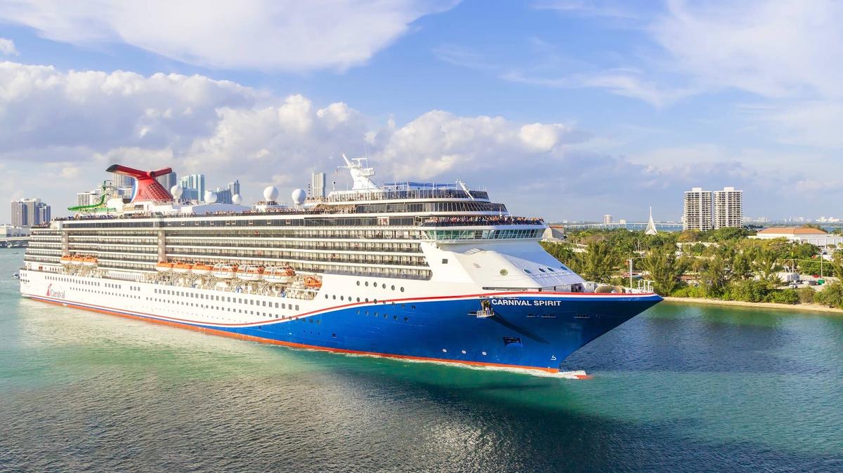 The Carnival Spirit cruise ship is sailing from port in Miami on a sunny day.