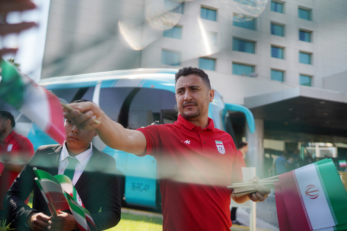 Soccer Football - FIFA World Cup 2026 - Iran leave Tijuana hotel ahead of first World Cup match - Tijuana, Mexico - June 14, 2026 An official gives out Iran flags to fans outside the hotel REUTERS/Victor Medina