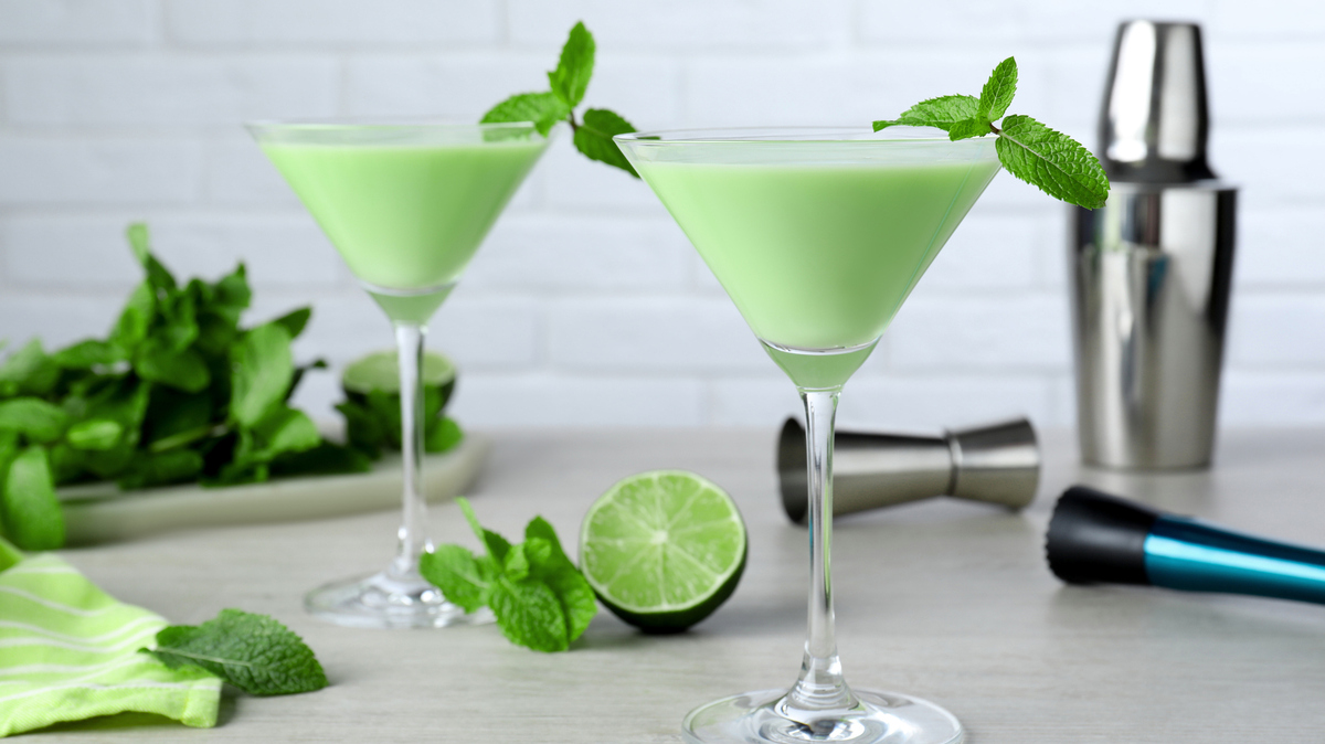 Delicious mint liqueur with green leaves on white wooden table