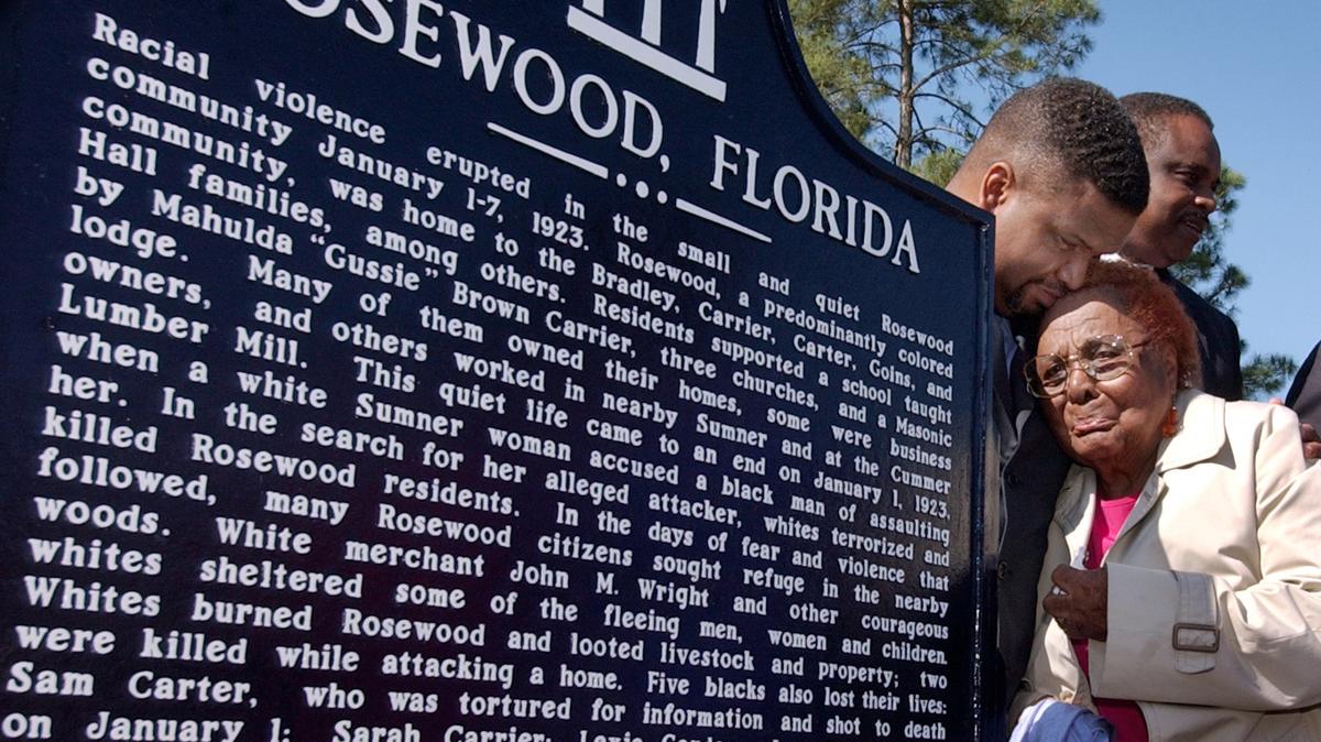 In this Tuesday, May 4, 2004 file photo, a survivor of the 1923 racial violence in Rosewood, Robie Allenetta Mortin, is comforted by Florida Rep. Ed Jennings Jr. after he unveiled a historical marker at a dedication ceremony. In 1994, the Florida Legislature was the first in the country to approve reparations, $2.1 million for the 11 survivors living at that time.
