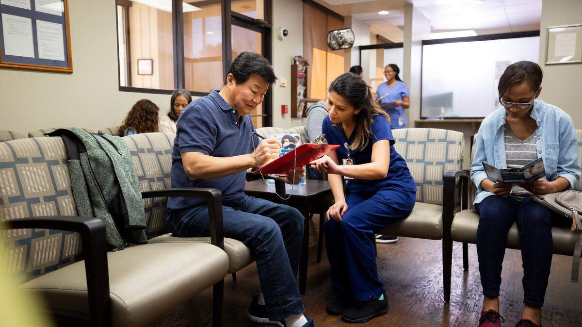 Mid adult nurse helps a senior man fill out a medical form as he waits to be seen by a doctor.