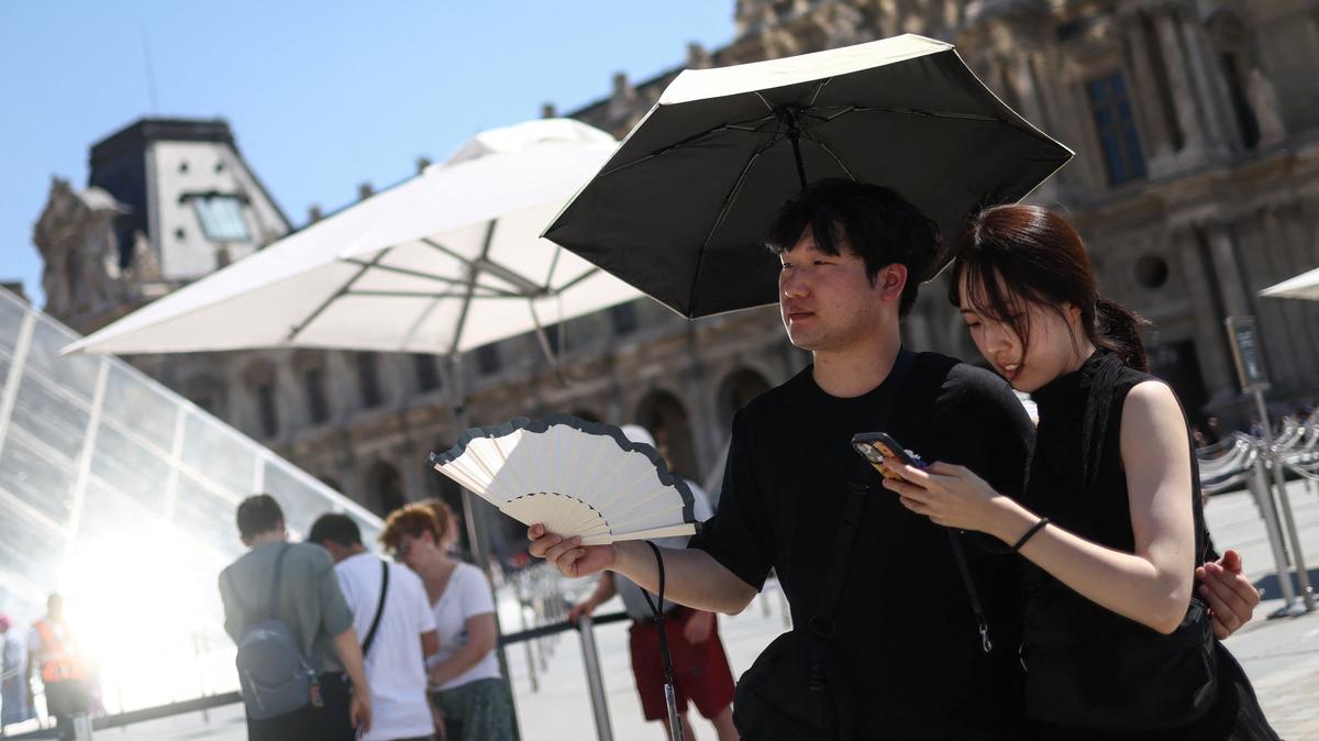 Two people shelter under an umbrella and use a fan outside the Louvre amid a severe heat wave in Paris, France, May 27, 2026. REUTERS/Tom Nicholson