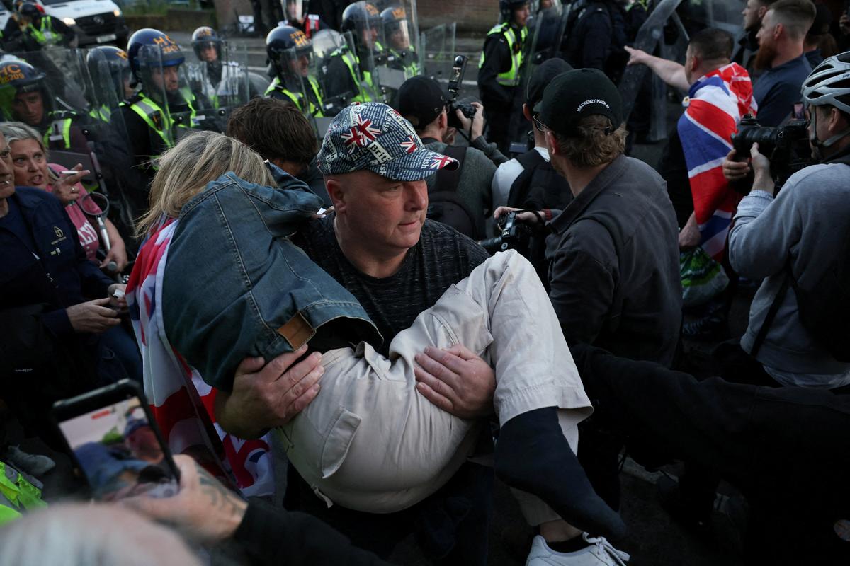 A protester carries a way a woman during a demonstration following the conviction of Vikrum Digwa for the murder of student Henry Nowak, with police officers standing guard in the background, in Southampton, Britain, June 2, 2026. REUTERS/Isabel Infantes     TPX IMAGES OF THE DAY