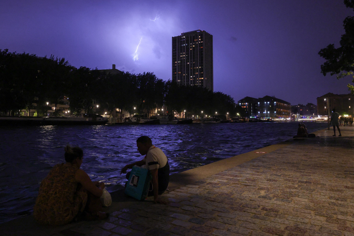 People sit on the banks of the Bassin de la Villette during a storm, as lightning strikes behind them amid a heatwave in Paris, France, June 27, 2026. REUTERS/Tom Nicholson