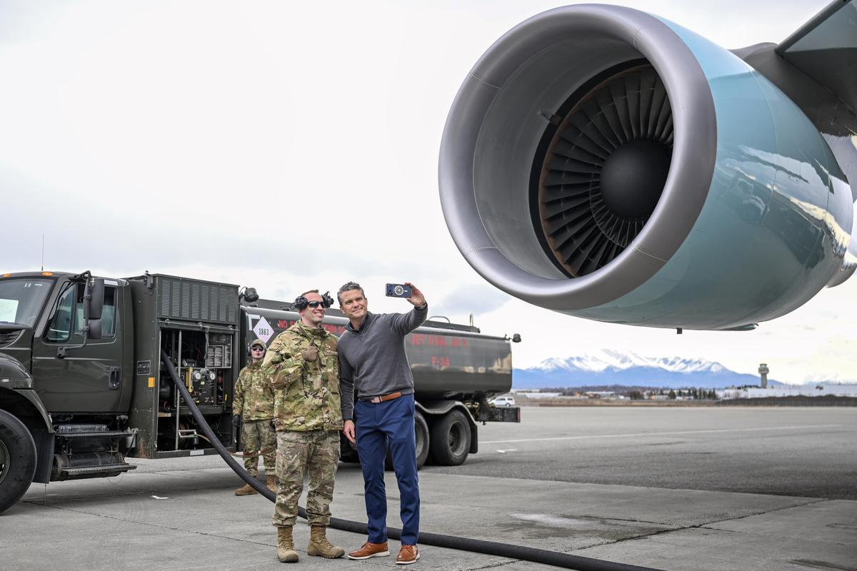 Defense Secretary Pete Hegseth poses with U.S. service members as Air Force one, en route to Beijing, stops for refueling at Ted Stevens Anchorage International Airport in Anchorage, Alaska, on Tuesday, May 12, 2026. President Donald Trump arrived in Beijing on Wednesday for a two-day summit with China's leader, Xi Jinping. (Kenny Holston/The New York Times)