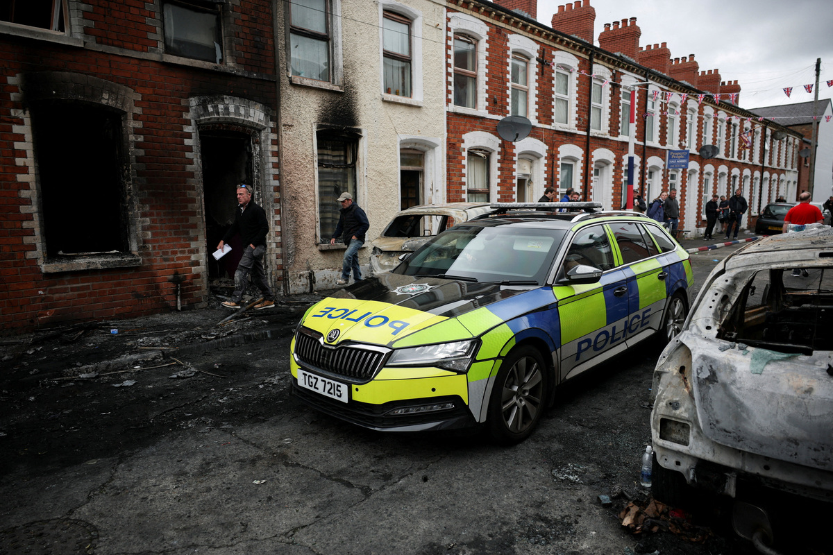 A police car drives past a burnt building on a debris-strewn street, in the aftermath of anti-immigrant protests following a knife attack on June 8, which left a man seriously injured and prompted police to declare a critical incident, at Lendrick Street, east Belfast, Northern Ireland, June 10, 2026. REUTERS/Isabel Infantes