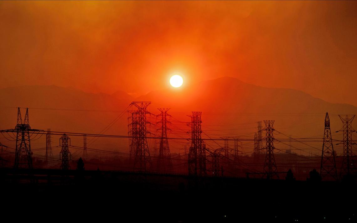 Smoke from a wildfire floats over power lines as the sun rises in Newhall in 2019. Delays in building new power lines may slow California’s efforts to make its energy supply greener.