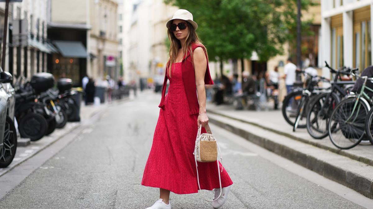PARIS, FRANCE - APRIL 18: Maria Rosaria Rizzo wears long straight brown hair partially covered with a beige Borsalino hat, oversized black sunglasses, a red Mango sleeveless midi dress, a red Moschino sweater worn over the shoulders, a Chloe straw bag with white leather straps, and white Lacoste tennis sneakers shoes, during a street style fashion photo session, on April 18, 2026 in Paris, France. (Photo by Edward Berthelot/Getty Images)