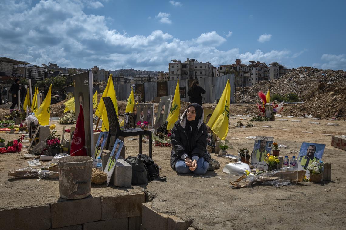 A woman sits near Hezbollah flags as she mourns by the grave of a loved one at a temporary cemetery in Beirut, Lebanon, on April 13, 2026. According to the Lebanese government, more than 2,000 people have been killed in the country since the Iran-backed militia Hezbollah fired on northern Israel in early March, prompting a widening Israeli ground invasion. (Diego Ibarra Sánchez/The New York Times)