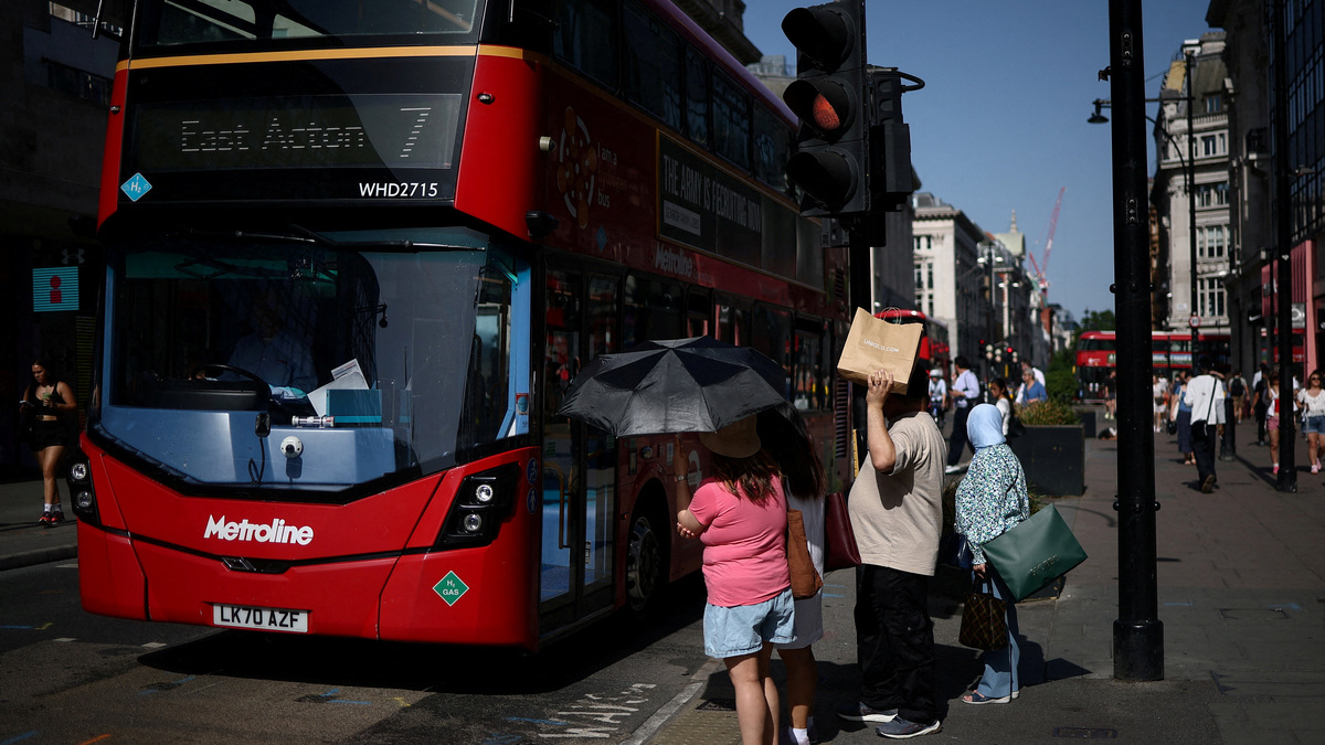FILE PHOTO: People use umbrellas and shopping bags to shield themselves from the sun while waiting to cross Oxford Street as Britain experiences record temperatures disrupting schools and transport networks, in London, Britain, June 23, 2026. REUTERS/Guglielmo Mangiapane/File Photo