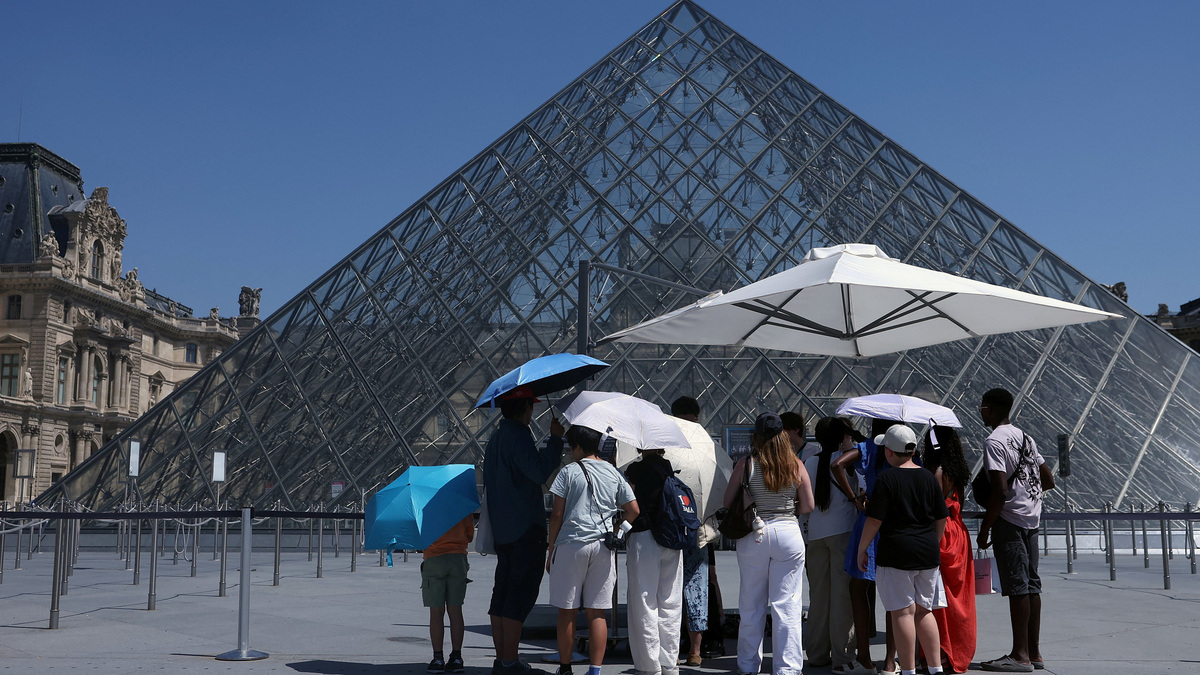 Tourists stand under umbrellas to protect themselves from the sun in front of the glass Pyramid of the Louvre museum as the museum closes early due to the heatwave as temperatures rise in Paris, France, June 24, 2026. REUTERS/Alice Sacco