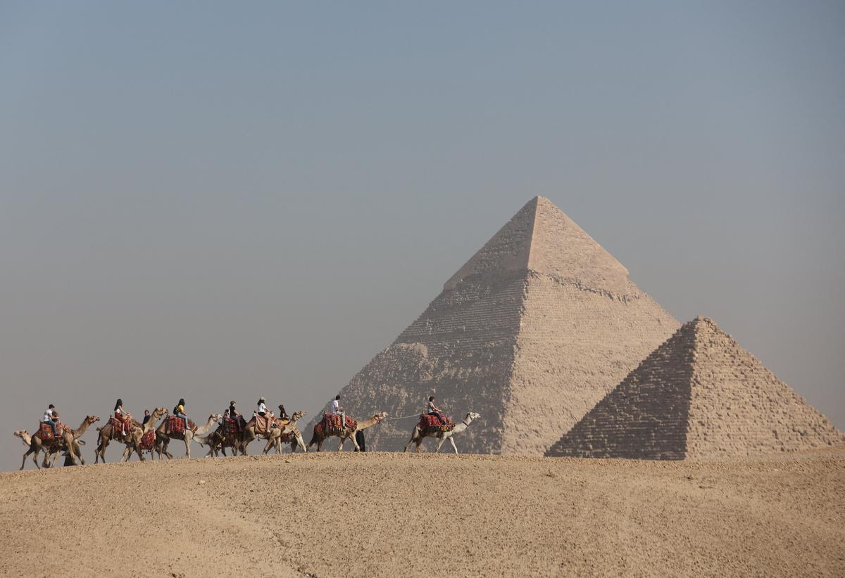 FILE PHOTO: Tourists ride camels in front of the Great Pyramids plateau in Giza, Egypt December 11, 2022. REUTERS/Amr Abdallah Dalsh/File Photo