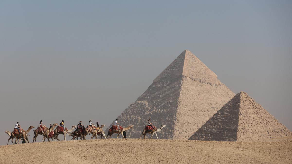 FILE PHOTO: Tourists ride camels in front of the Great Pyramids plateau in Giza, Egypt December 11, 2022. REUTERS/Amr Abdallah Dalsh/File Photo
