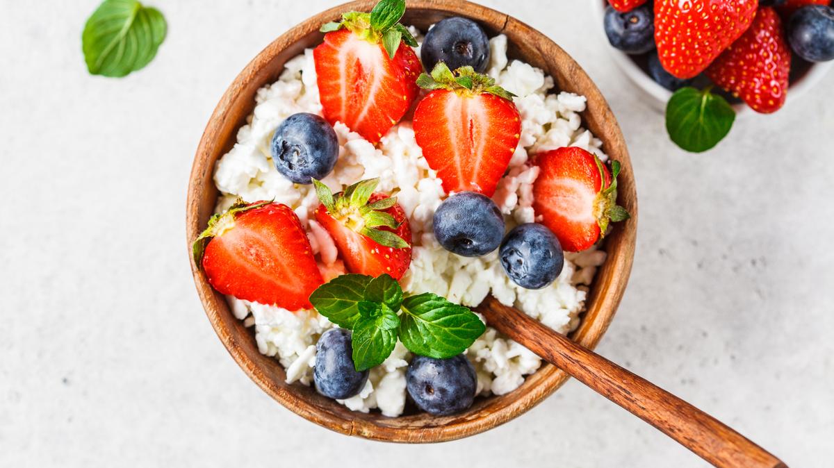Cottage cheese with strawberries and blueberries in a wooden bowl, light gray background.