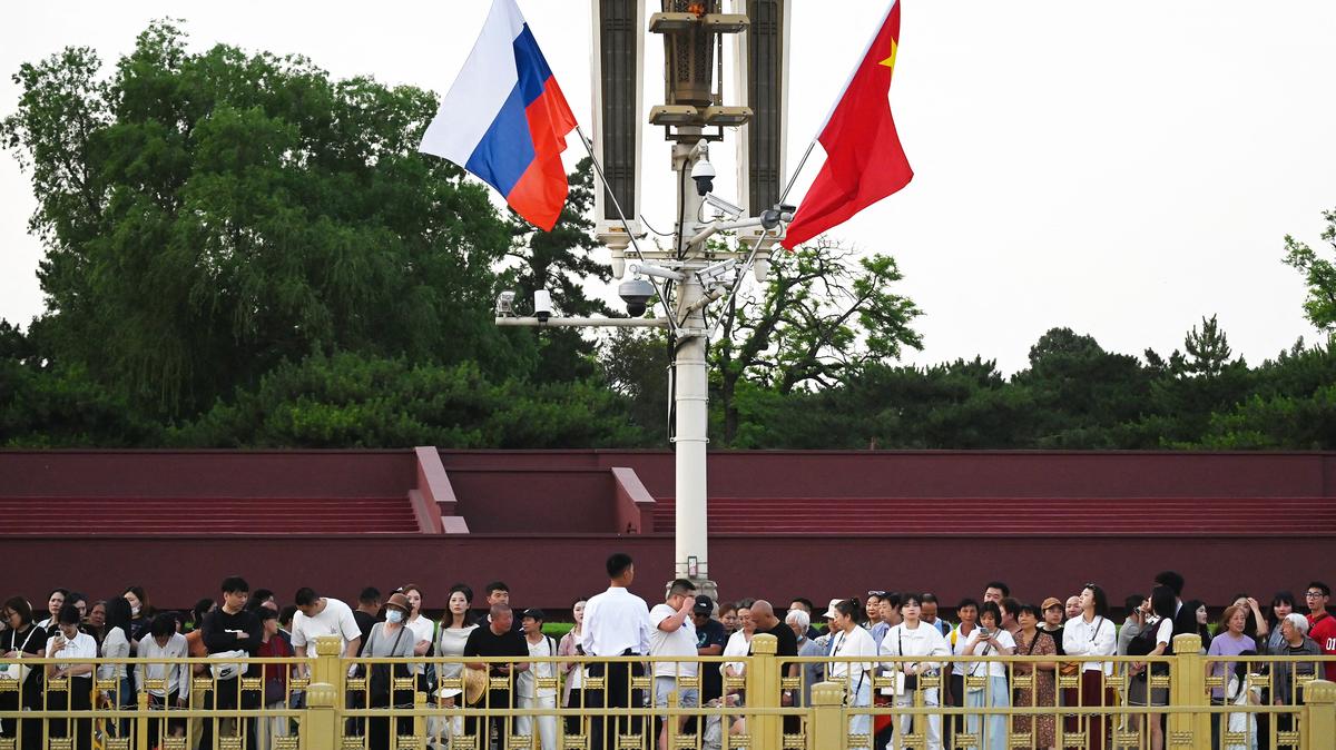 People wait for the daily flag lowering ceremony, below the Russian, left, and Chinese flags flying in Tiananmen Square in Beijing on May 19, 2026. Russian President Vladimir Putin arrived in Beijing on May 19 for talks with his Chinese counterpart and his "long-time good friend" Xi Jinping, intending to show their ties are unshakeable days after a visit by U.S. President Donald Trump.