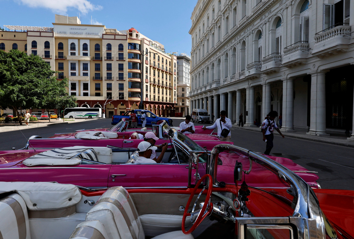 Taxi drivers of vintage cars look at their mobile phones while waiting for clients at Central Park, as U.S. sanctions have led most major tourism and travel companies to leave the island or drastically scale back their operations, in Havana, Cuba, June 8, 2026. REUTERS/Norlys Perez