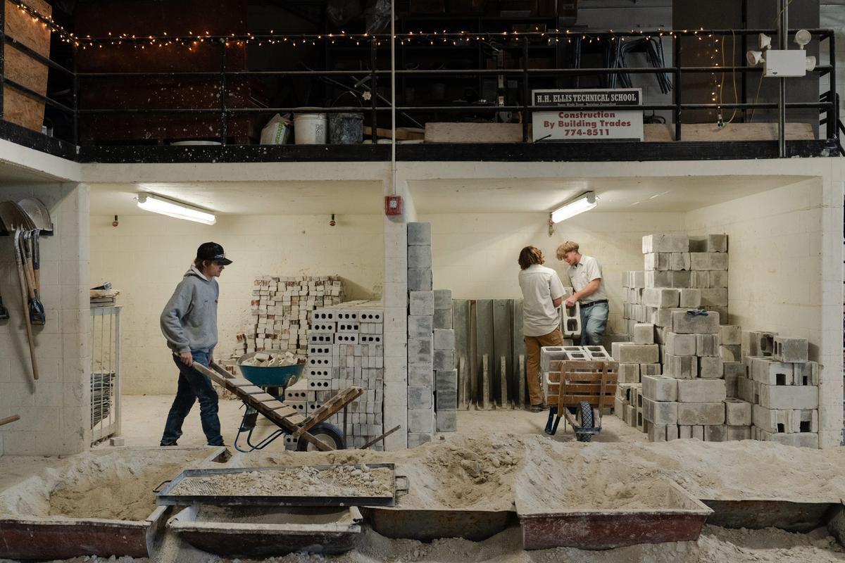  Noah Pillsbury, 17, (left) wheels a cart to move cinderblocks while working on a block pier in his masonry shop at Harvard H. Ellis Technical School in Danielson, CT on April 7, 2026. Credit: Sophie Park for The Hechinger Report