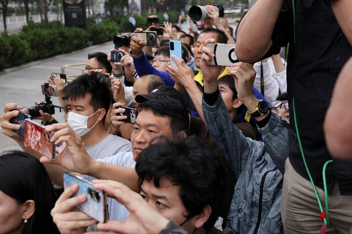People take photos from a side street as a motorcade believed to be carrying U.S. President Donald Trump drives past during his visit to China in Beijing, China, May 15, 2026. REUTERS/Go Nakamura