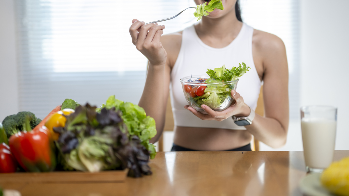 A stock image shows a young woman enjoying a fresh vegetable salad. 