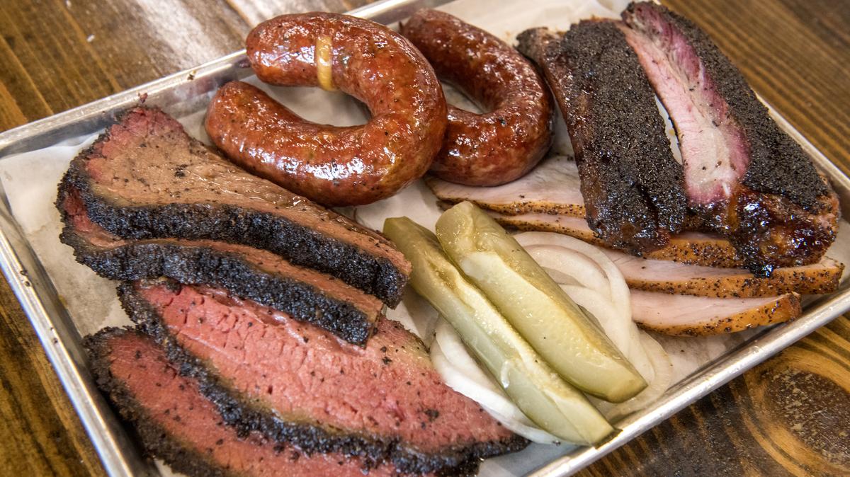 Close-up of a plate of barbecued meats at Mum Foods Smokehouse and Delicatessen, Austin, Texas, June 16, 2023. Pictured are, clockwise from top center, sausage, pork ribs, smoked turkey, onions, pickles, sliced pastrami, and sliced brisket. (Photo by John Anderson/The Austin Chronicle/Getty Images). 