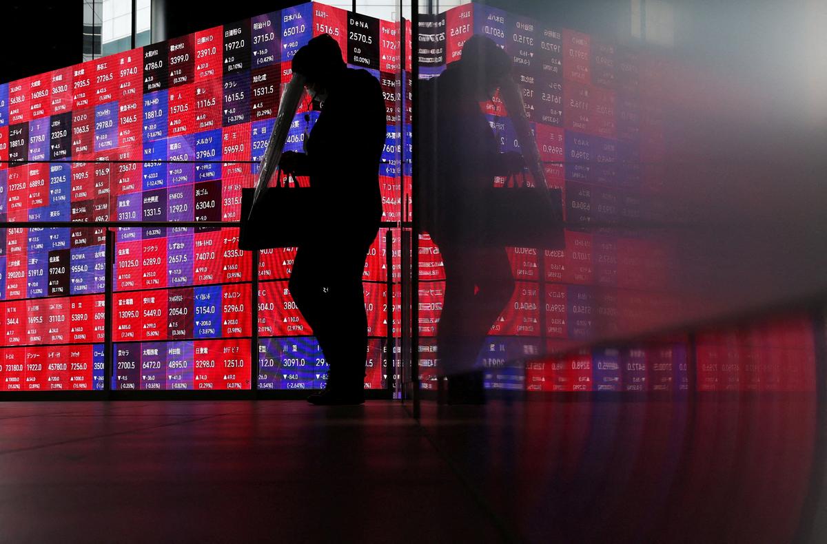 FILE PHOTO: A man walks in front of an electronic screen displaying Japan's Nikkei stock prices quotation board inside a conference hall in Tokyo, Japan, April 27, 2026. REUTERS/Issei Kato/File Photo