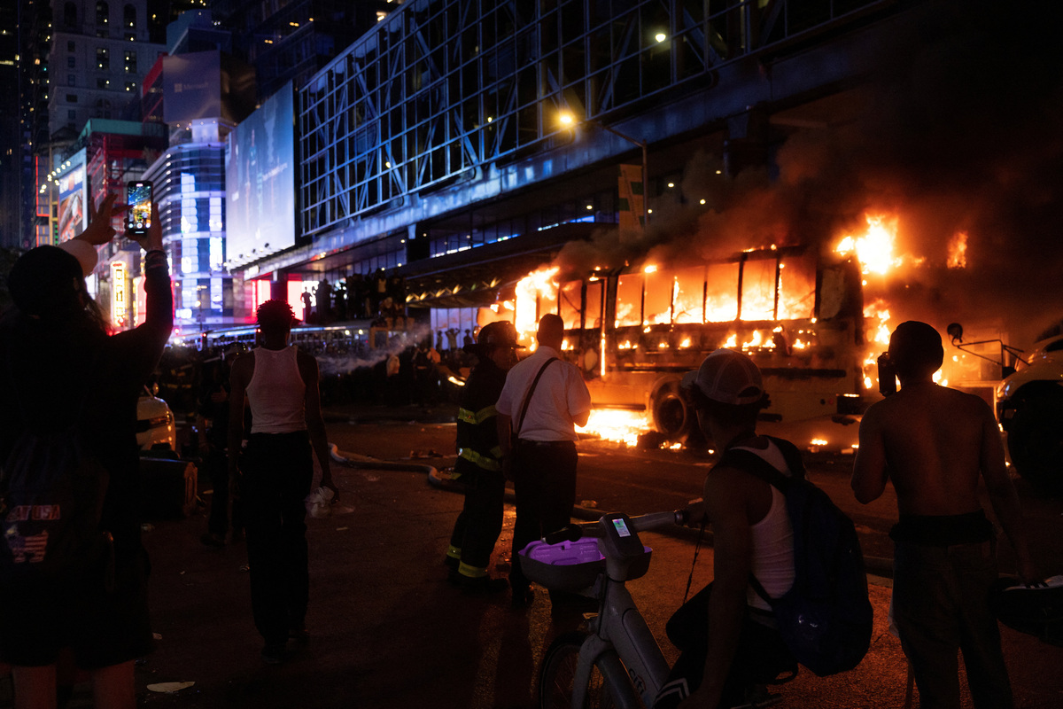 People stand near a shuttle bus outside the Port Authority Bus Terminal, after it burned amid celebrations over the New York Knicks' win over the San Antonio Spurs and World Cup festivities in New York, U.S., June 14, 2026. The shuttles had been brought in to transport spectators to and from the New York/New Jersey stadium for the World Cup. REUTERS/Ed Ou