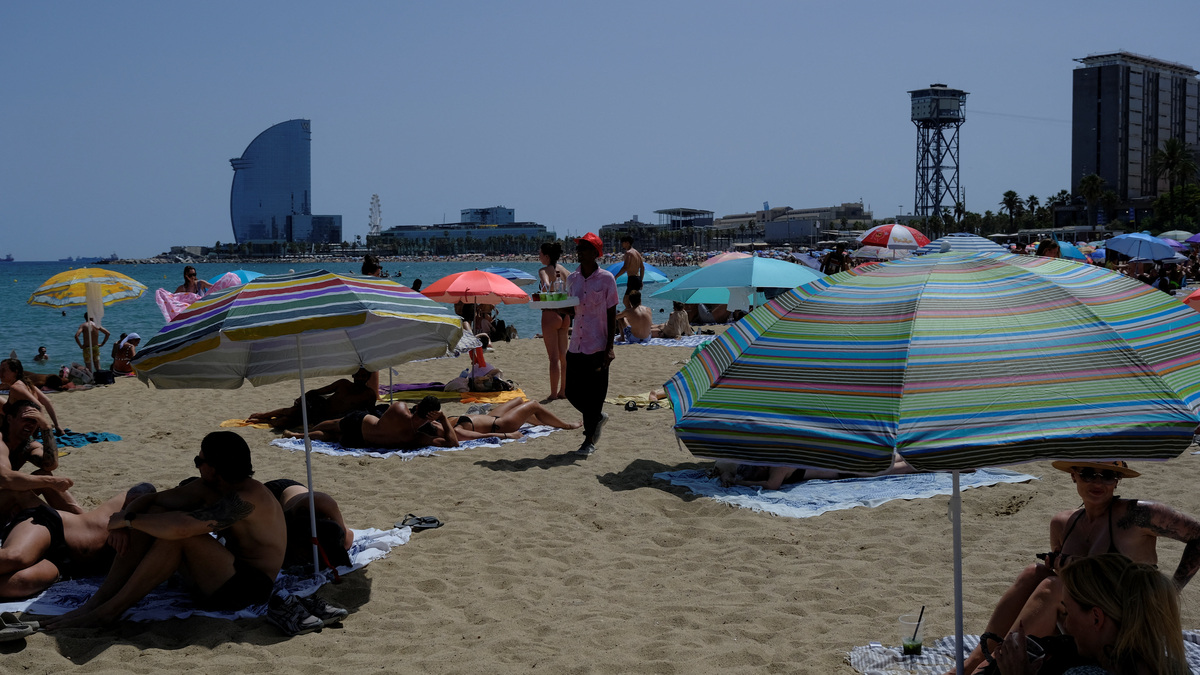 A man sells drinks for tourists and locals as they enjoy a Barcelona beach as temperatures rise during a heatwave affecting a large part of Spain on Sunday.