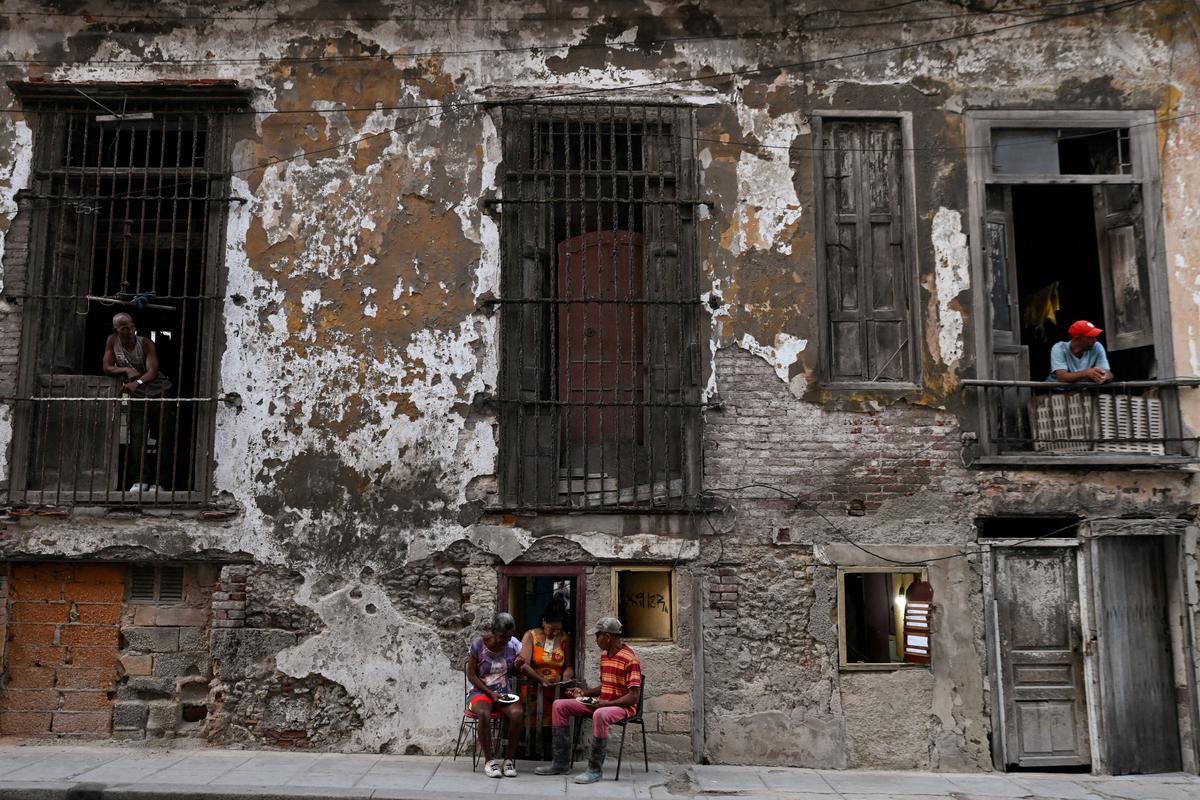 People eat outside of a small cafeteria while neighbors look out from a balcony, as Cuba's state-run economy has descended into a full-blown crisis after the administration of U.S. President Donald Trump hardened sanctions and cut off the Caribbean nation's oil supply, in Havana, Cuba February 21, 2026. REUTERS/Norlys Perez