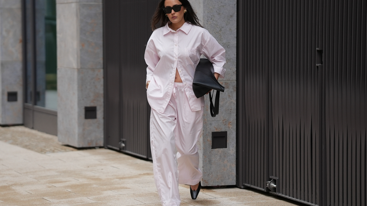 HAMBURG, GERMANY - MAY 5: Laura Noltemeyer is seen wearing a light pink pinstriped two-piece set consisting of an oversized cotton shirt and matching wide-leg trousers by Aylin Koenig; black leather square-toe heels with a sculptural deep-cut front detail by Aylin Koenig; a black Loewe "Puzzle Fold Tote Bag"; oversized black sunglasses by Celine; nude-colored fingernails; gold jewelry by H&M and COS consisting of statement earrings, bangles and rings; natural makeup; her dark brown hair is worn in soft waves with a middle part on May 5, 2026 in Hamburg, Germany. (Photo by Moritz Scholz/Getty Images)