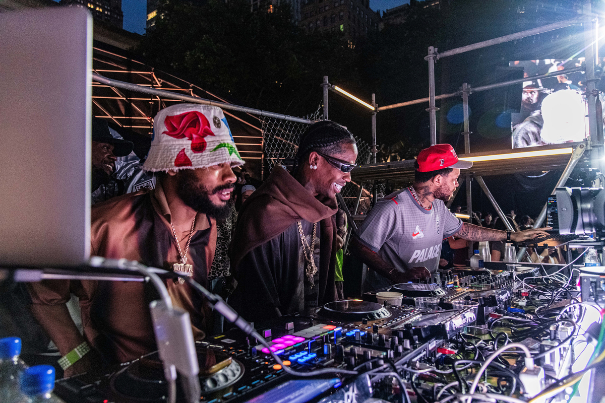 Rapper Travis Scott, center, smiles behind a DJ booth during a Nike Toma soccer event in New York on June 27, 2026. As World Cup matches take place across the United States, Nike and Adidas, the two largest sportswear companies in the world, are spending millions of dollars in a duel over the future of soccer in America. (Emma Rose Milligan/The New York Times)