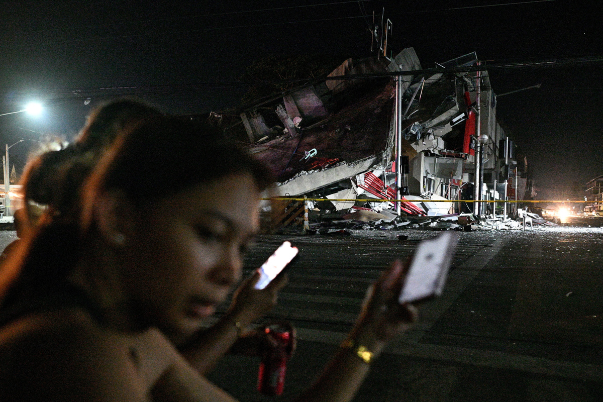 People use their phones near a collapsed building following the magnitude 7.8 quake in General Santos, southern Philippines, June 8, 2026. REUTERS/Noel Celis