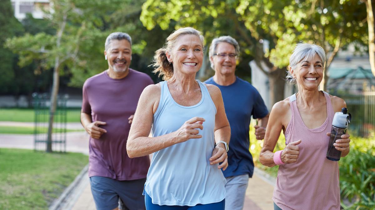 Group of happy older friends jogging in a city park. Fitness seniors running together outdoors while smiling. Mature multiethnic men and women enjoying a healthy morning workout.