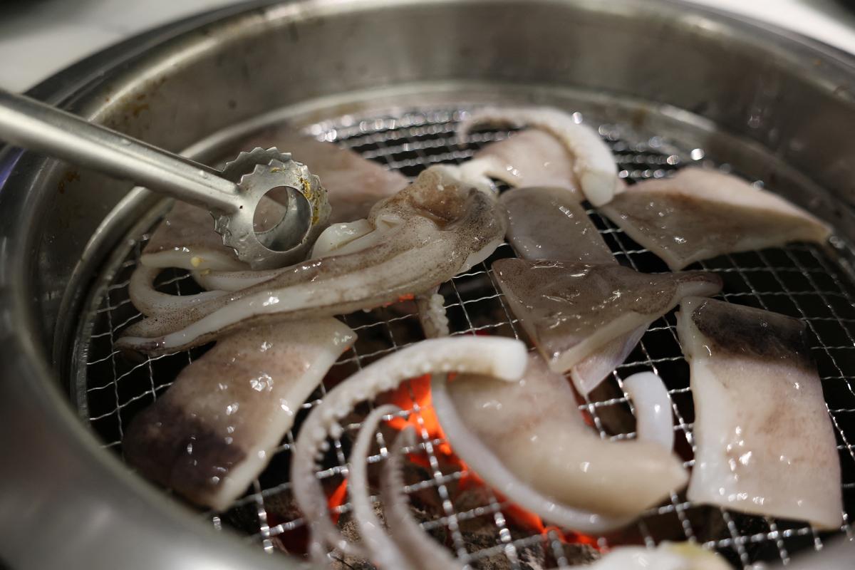 An employee cooks pieces of an Argentine squid ordered by a Reuters journalist over a charcoal grill at a restaurant in Beijing, China, March 27, 2026. REUTERS/Tingshu Wang